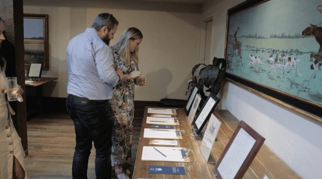 Two people examining documents and framed items on a table in a room.